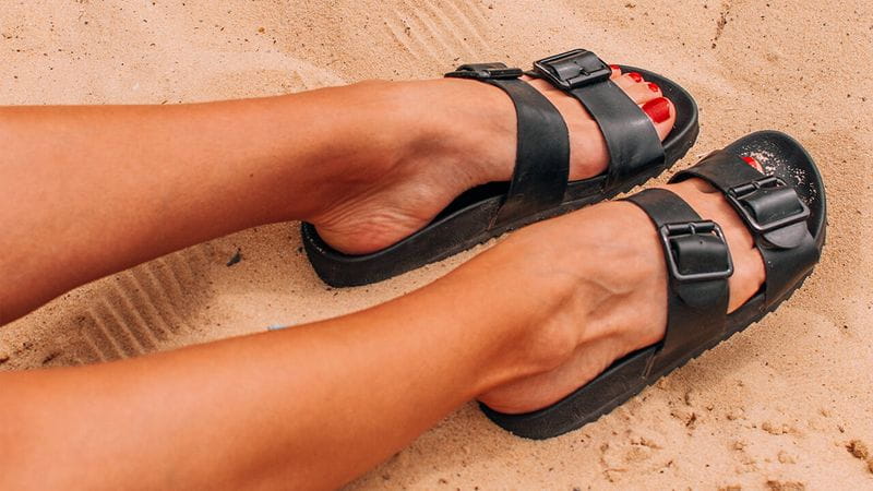 Pés de uma mulher com uma sandália preta na areia