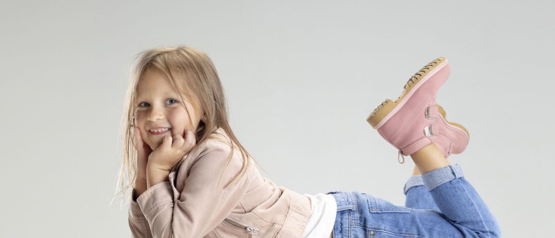 Imagem de uma menina, deitada de barriga para baixo, vestindo roupas confortáveis com um tênis rosa.