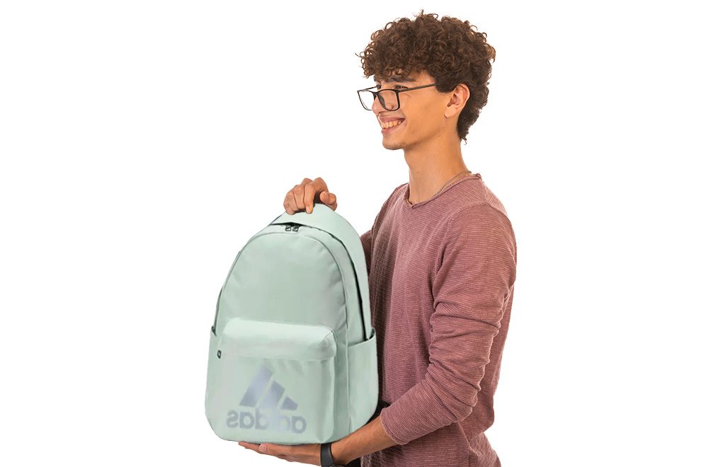 um menino segurando uma mochila da adidas verde claro em um fundo branco 