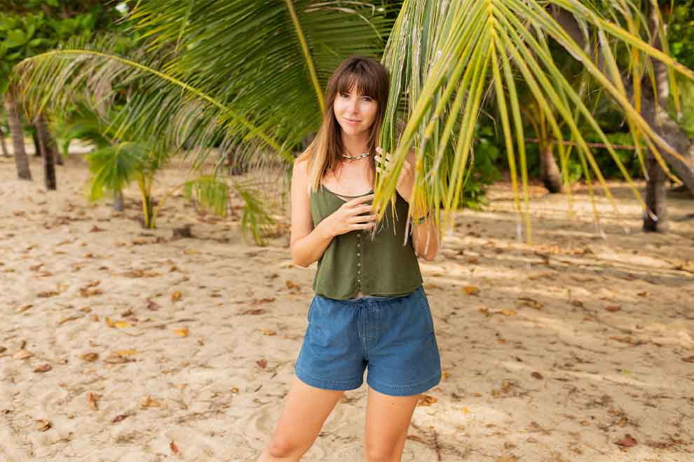 mulher usando um shorts jeans de cintura alta e uma blusa regata verde solta em uma praia