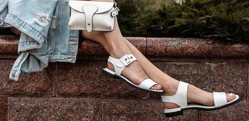 Sandália branca elegante com bolsa branca ao fundo