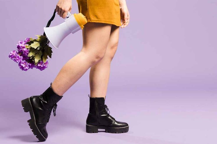 Mulher caminhando com megafone e flores roxas.