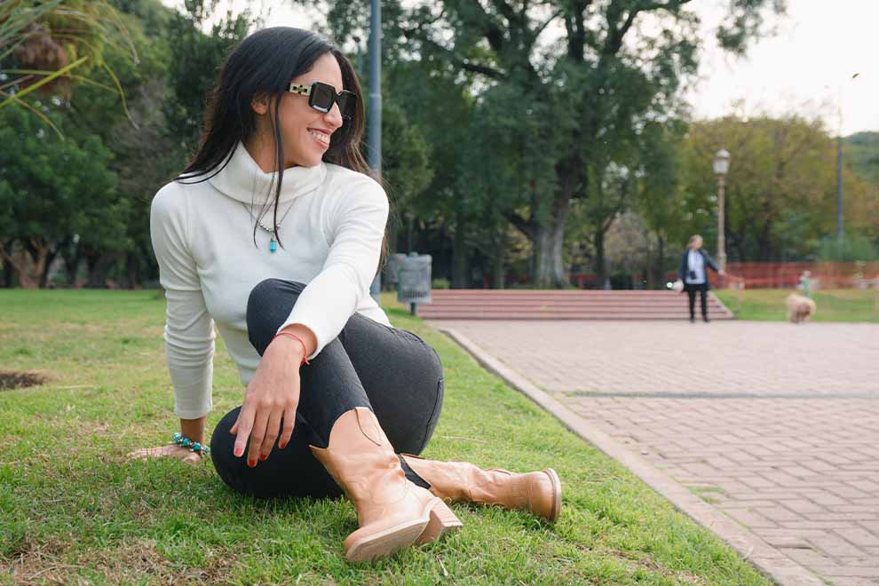 Mulher sorrindo sentada em parque com roupas modernas.