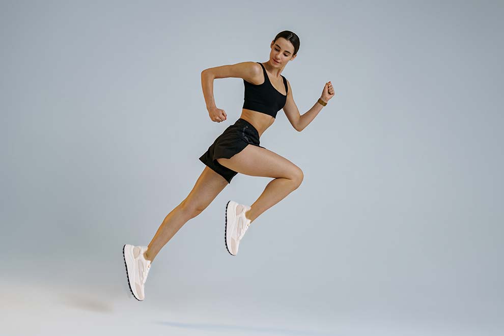 Mulher correndo em fundo neutro, vestindo roupa de treino.