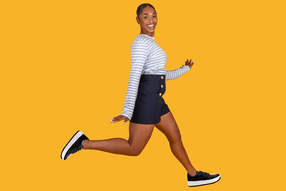 Mulher sorrindo e pulando em fundo amarelo