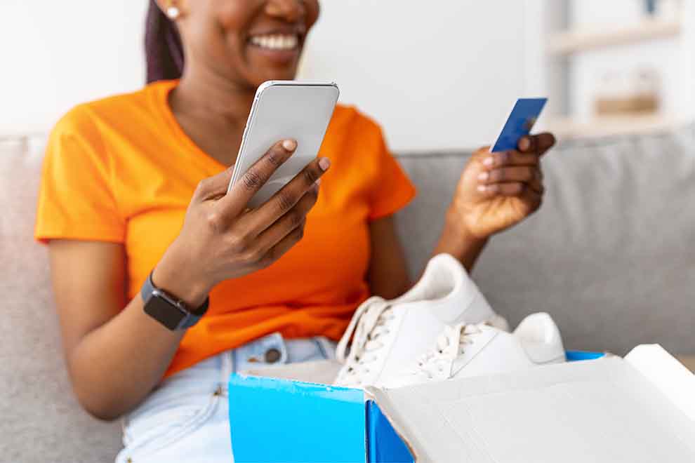Mulher sorridente fazendo compras online com celular e cartão.