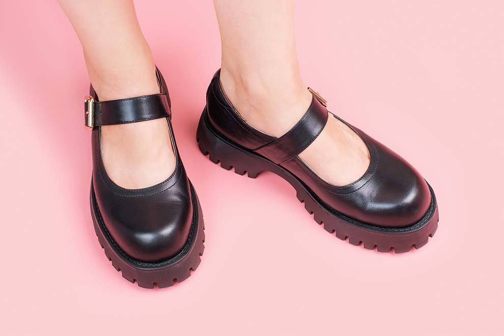 Sapatilha preta com detalhe de fivela sobre fundo rosa.
