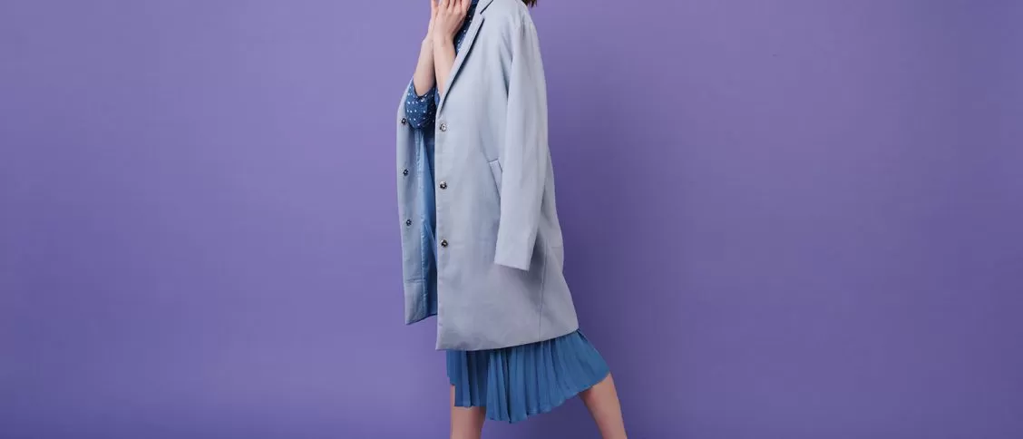 Imagem de uma modelo feminina vestindo um vestido azul com casaco e tênis esportivo, com o fundo roxo