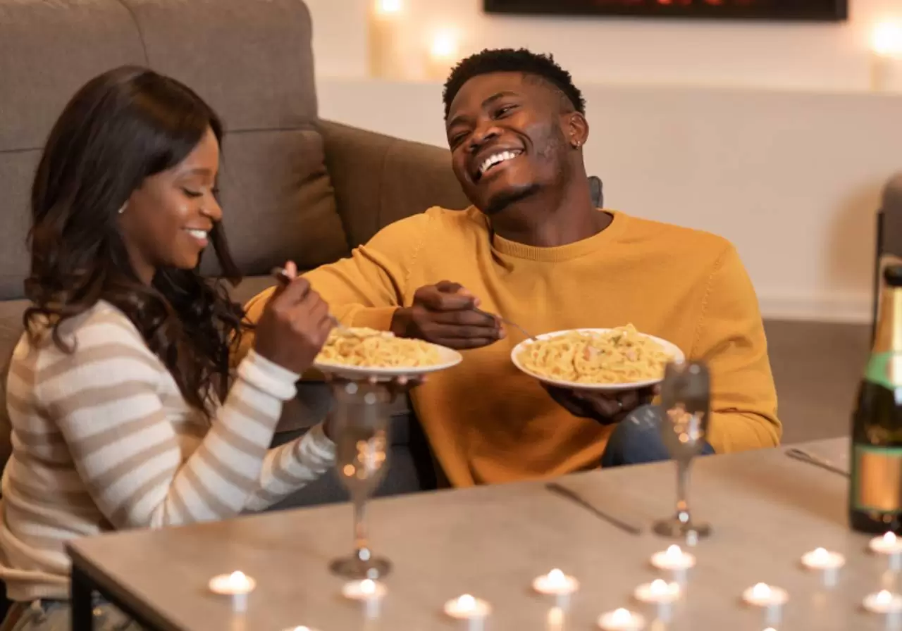 casal negro comendo macarrão em jantar romântico em casa