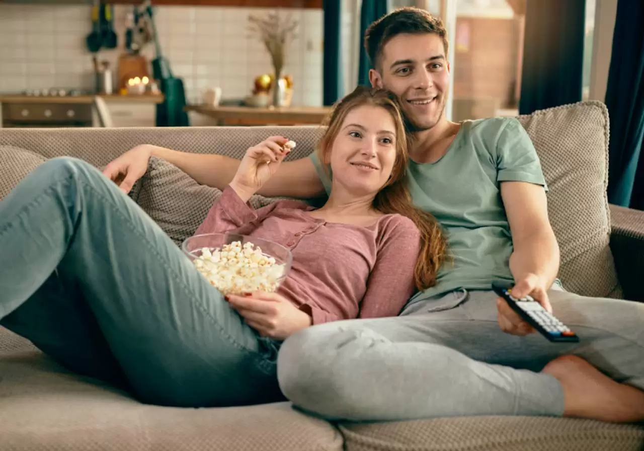 casal sorridente comendo pipoca e assistindo tv no sofá