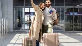 casal feliz em frente ao aeroporto com malas e passaporte