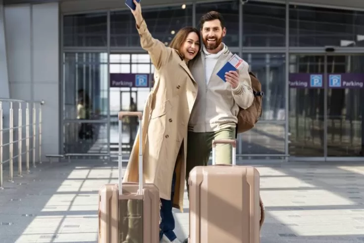 casal feliz em frente ao aeroporto com malas e passaporte
