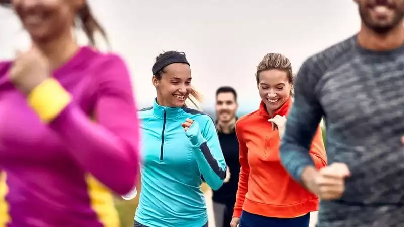 Duas mulheres correndo em foco na foto que tem cinco pessoas.