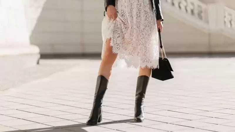 Combinar bota Imagem apenas da cintura para baixo, moça com vestido branco, blusa preta e uma bota preta.