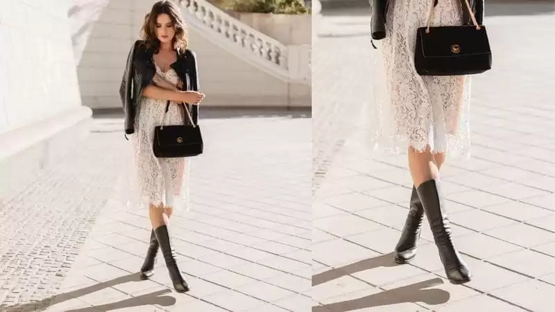 Moça com vestido branco, blusa preta e uma bota preta.