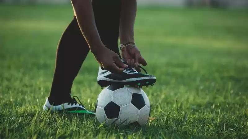 pessoa com pé em cima da bola amarra o cadarço da sua chuteiras para futebol de campo