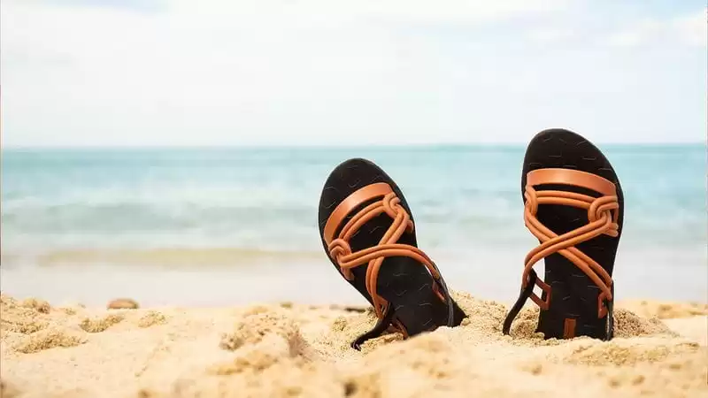 sandálias afundadas na areia de frente pro mar em um dia clara