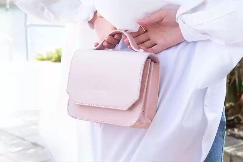 imagem de uma modelo de costas vestindo uma camisa branca, segurando uma bolsa de mão de cor rose pequena 