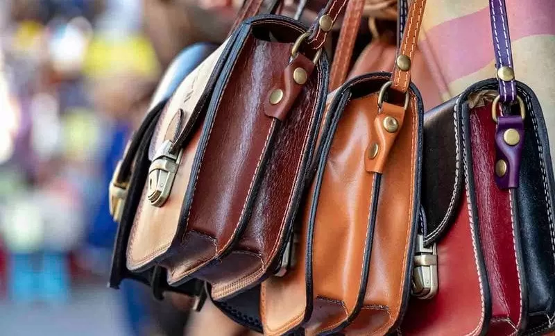 imagem com diversas bolsas de couro com alça de várias cores em um fundo desfocado