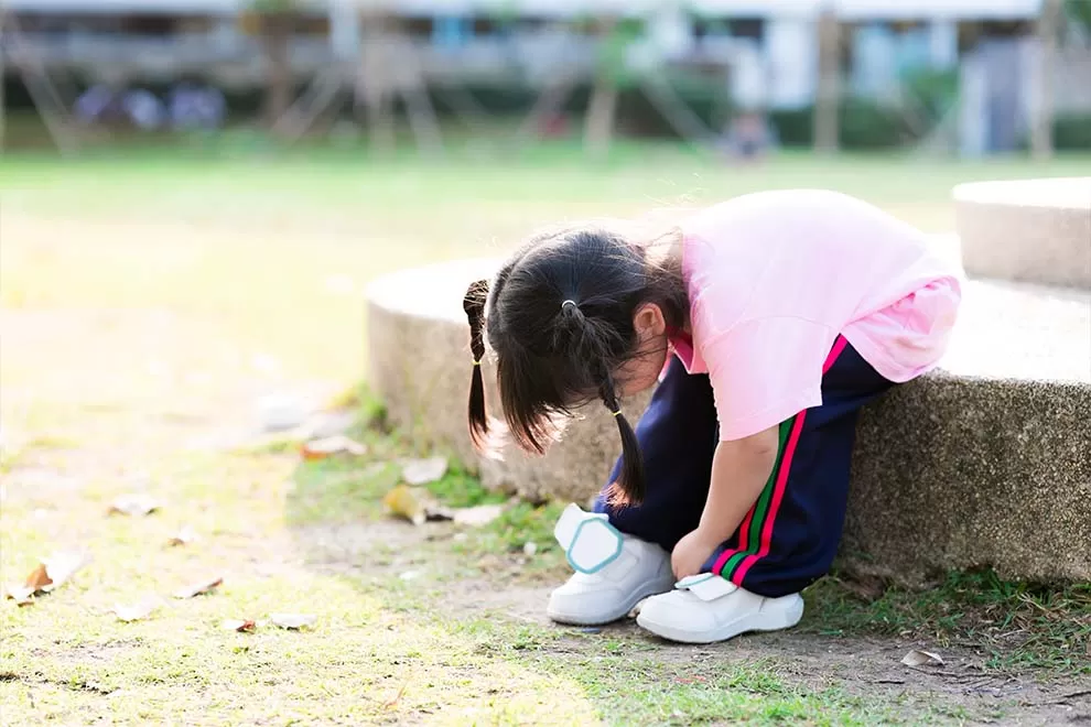 Menina amarrando um tênis branco em um parque durante o dia. 