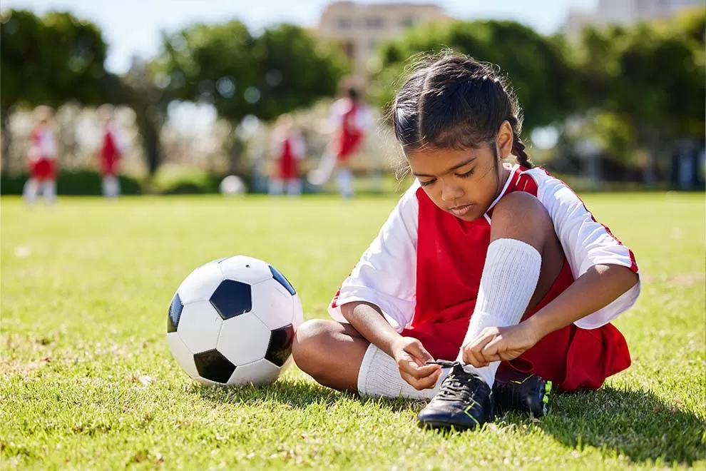 Menina amarrando a chuteira em um jogo de futebol 