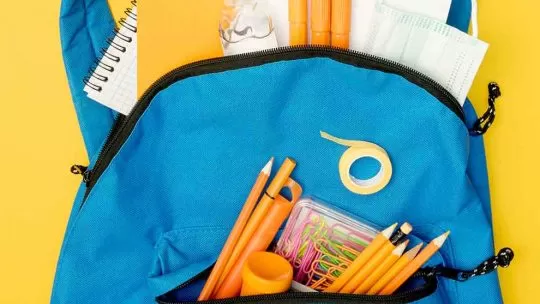 mochila azul com material escolar dentro e em um fundo amarelo
