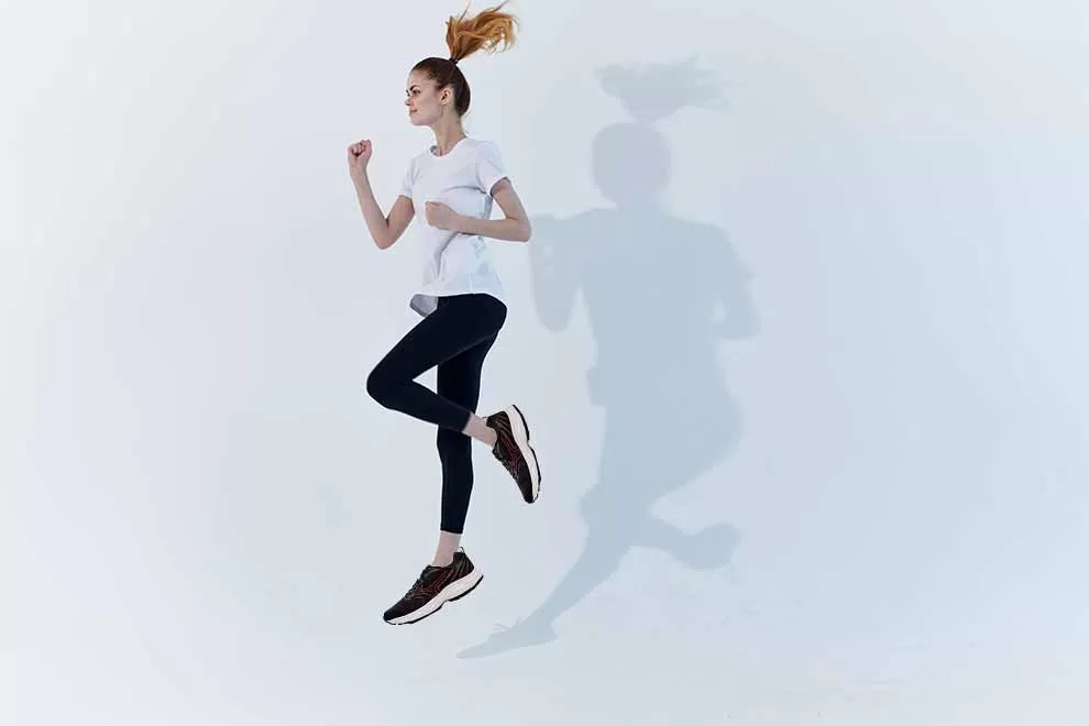 Mulher correndo em fundo branco, usando roupa esportiva.