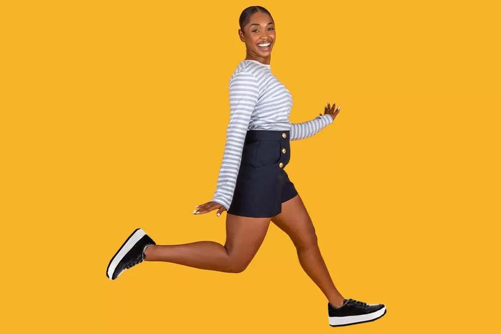 Mulher sorrindo e pulando em fundo amarelo