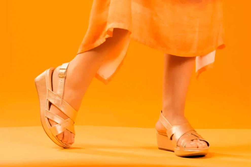 Sandália feminina de plataforma dourada em fundo laranja.
