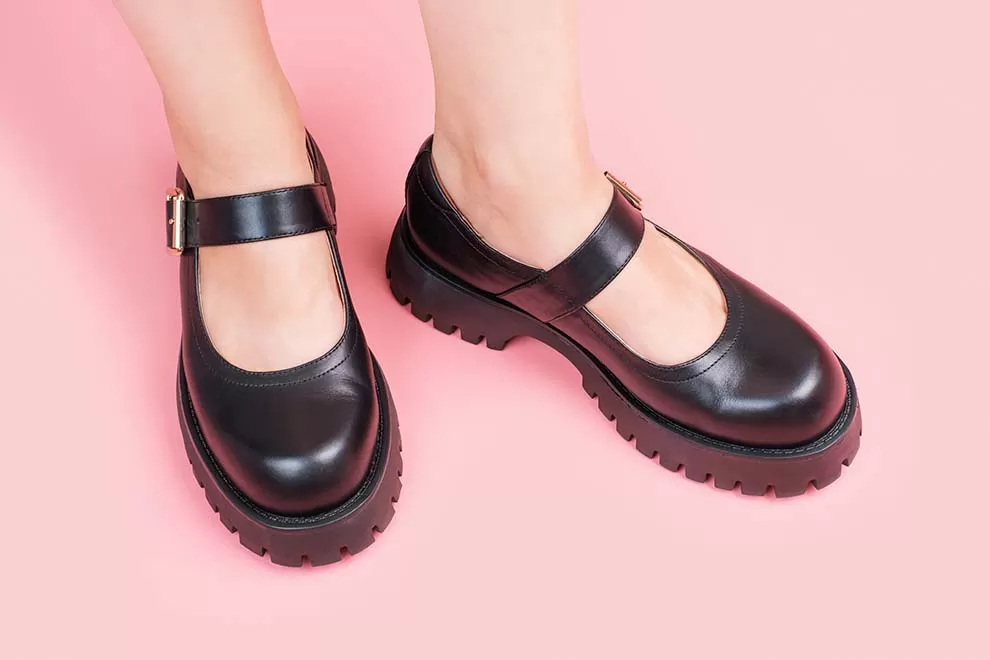 Sapatilha preta com detalhe de fivela sobre fundo rosa.